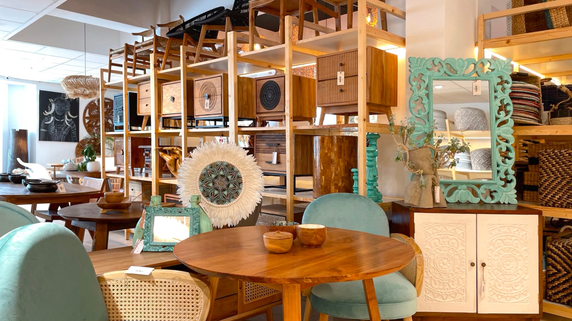 Mobilier din lemn masiv si lemn de tec, mese, scaune din ratan, oglinzi sculptate si decoratiuni din fibre naturale expuse in showroomul Komodo Casa, intr-o amenajare calda cu accente artizanale pentru living si dining.