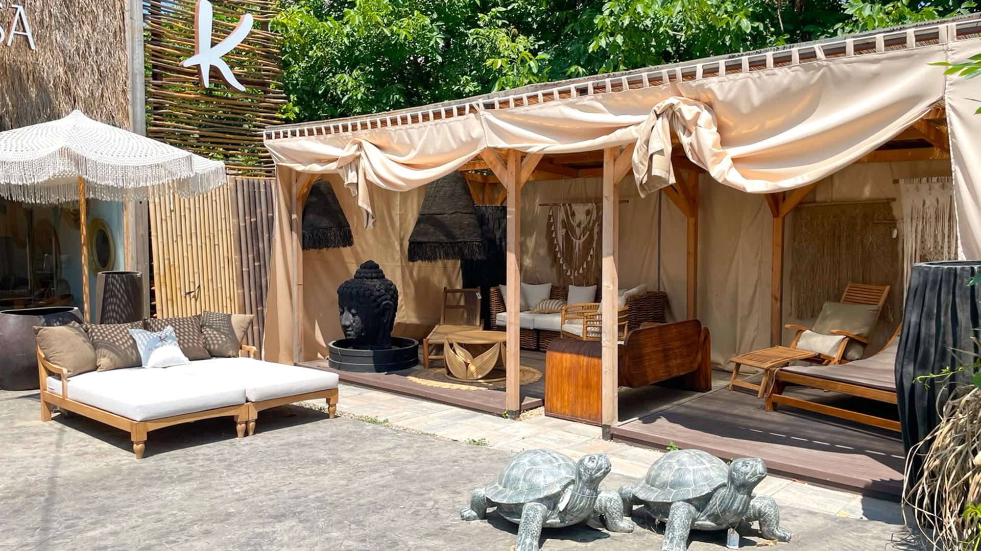 Mobilier de exterior din lemn de tec expus in showroomul Komodo Casa, cu sezlonguri, bambus, abajururi si decoratiuni din fibre naturale, macrame si fantani din fibrociment pentru terasa si gradina.